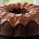 Close-up of a dark chocolate bundt cake with a swirled chocolate frosting on a black cake stand, representing a chocolate cream cheese pound cake gordon ramsay recipe.