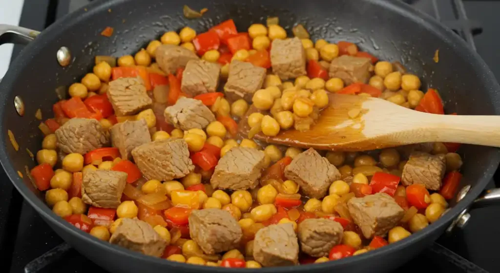 Terra Massoud Recipe: A top-down view of the dish with chickpeas, tofu, and red bell peppers being cooked in a pan.