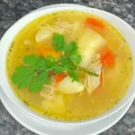 Finished bowl of Puerto Rican Chicken Noodle Soup garnished with parsley.