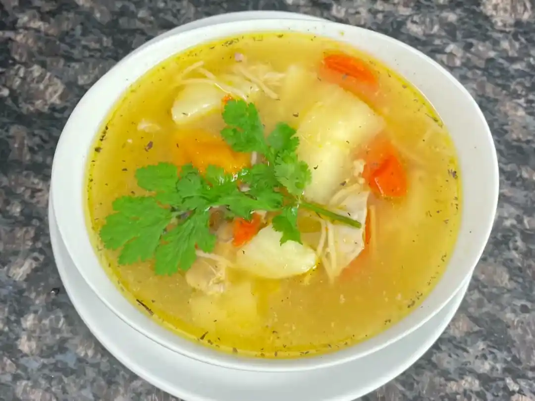 Finished bowl of Puerto Rican Chicken Noodle Soup garnished with parsley.