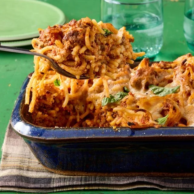 Baked spaghetti topped with cheese and herbs in a casserole dish