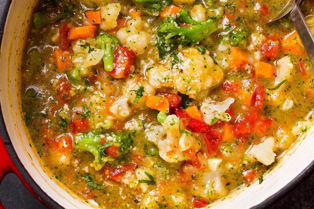 Creamy broccoli cauliflower soup topped with herbs in a bowl