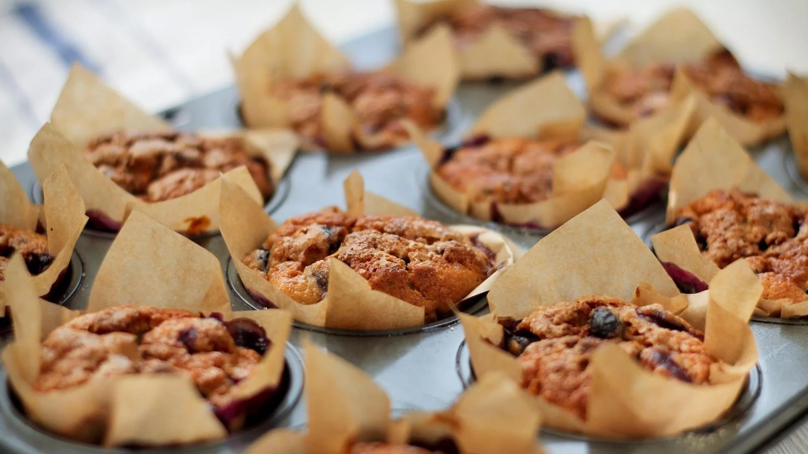 Freshly baked Cinnamon Banana Muffins with blueberries on a wooden table.
