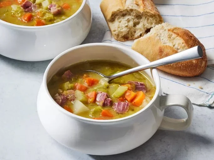 Bowl of cozy split pea soup garnished with herbs and bread on the side