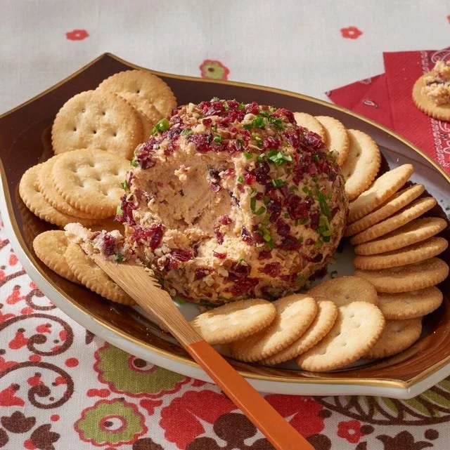 Cranberry-Pecan Cheese Ball decorated with nuts and cranberries on a serving platter