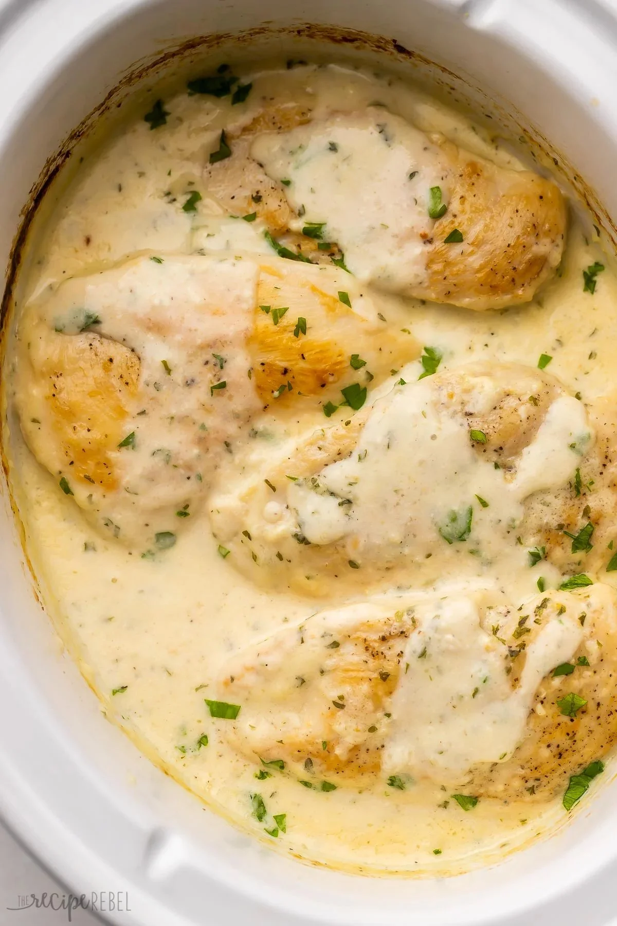 Crockpot creamy garlic chicken served with herbs and vegetables.