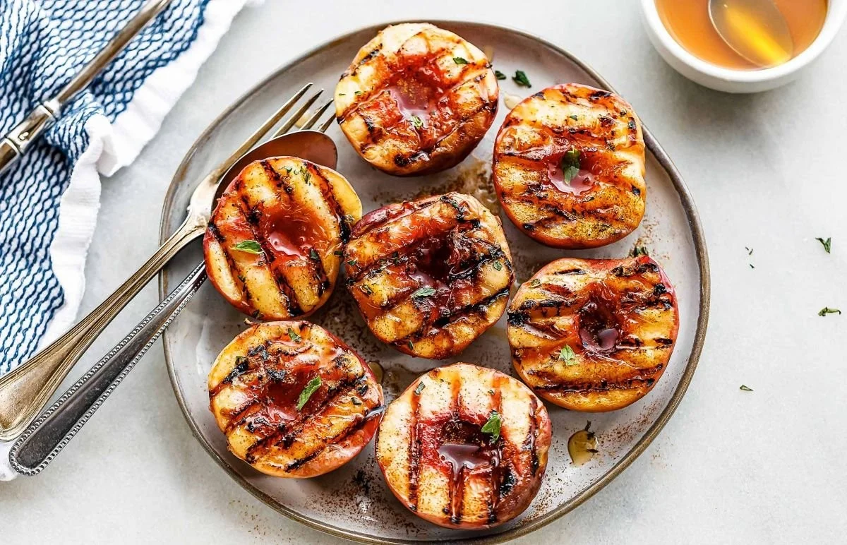 Grilled peaches drizzled with vanilla maple glaze on a serving plate.
