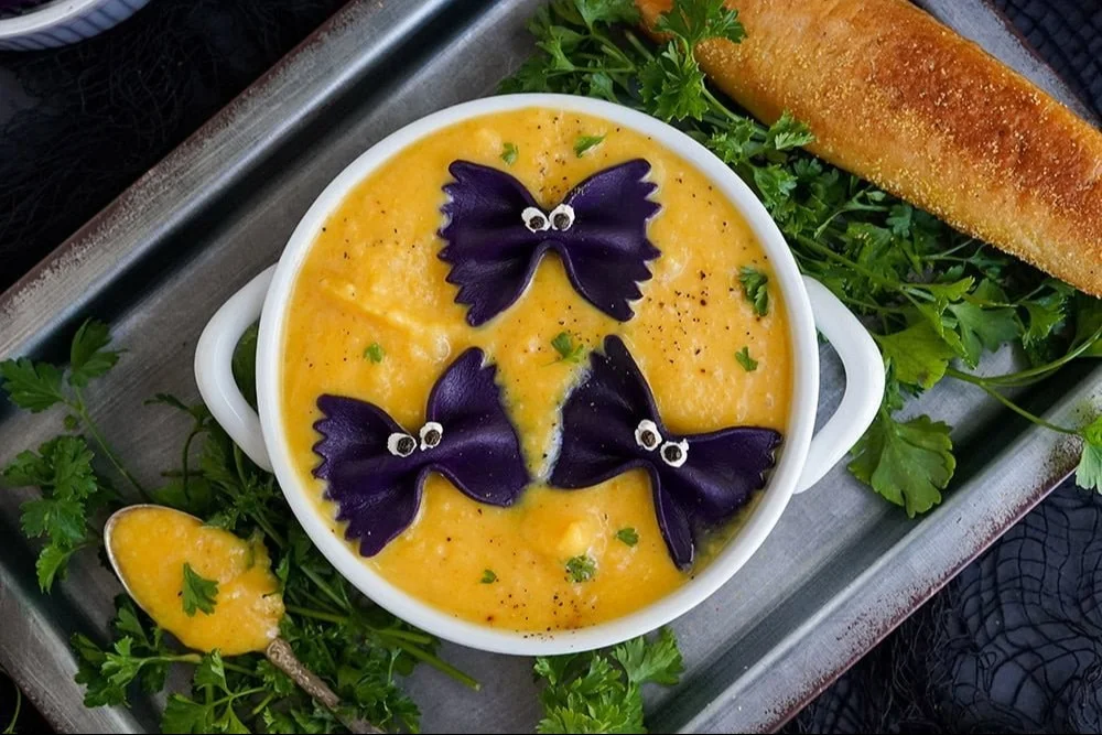 A bowl of Halloween butternut squash soup garnished with pumpkin seeds and herbs.