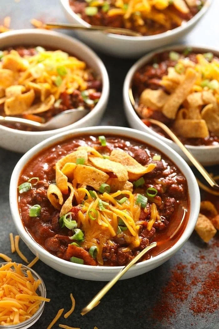 Bowl of homemade chili topped with cheese and herbs, served with cornbread.