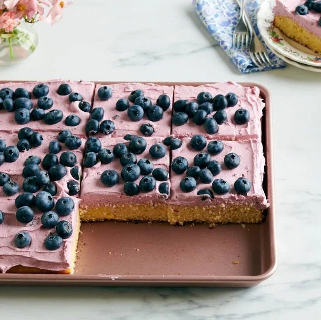 Slice of Lemon Blueberry Sheet Cake on a plate with lemon slices and blueberries.