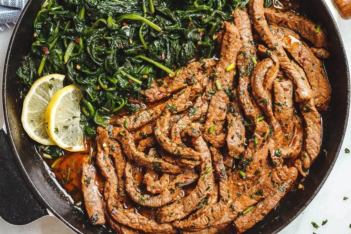 Lemon garlic butter steak served with fresh spinach on a plate