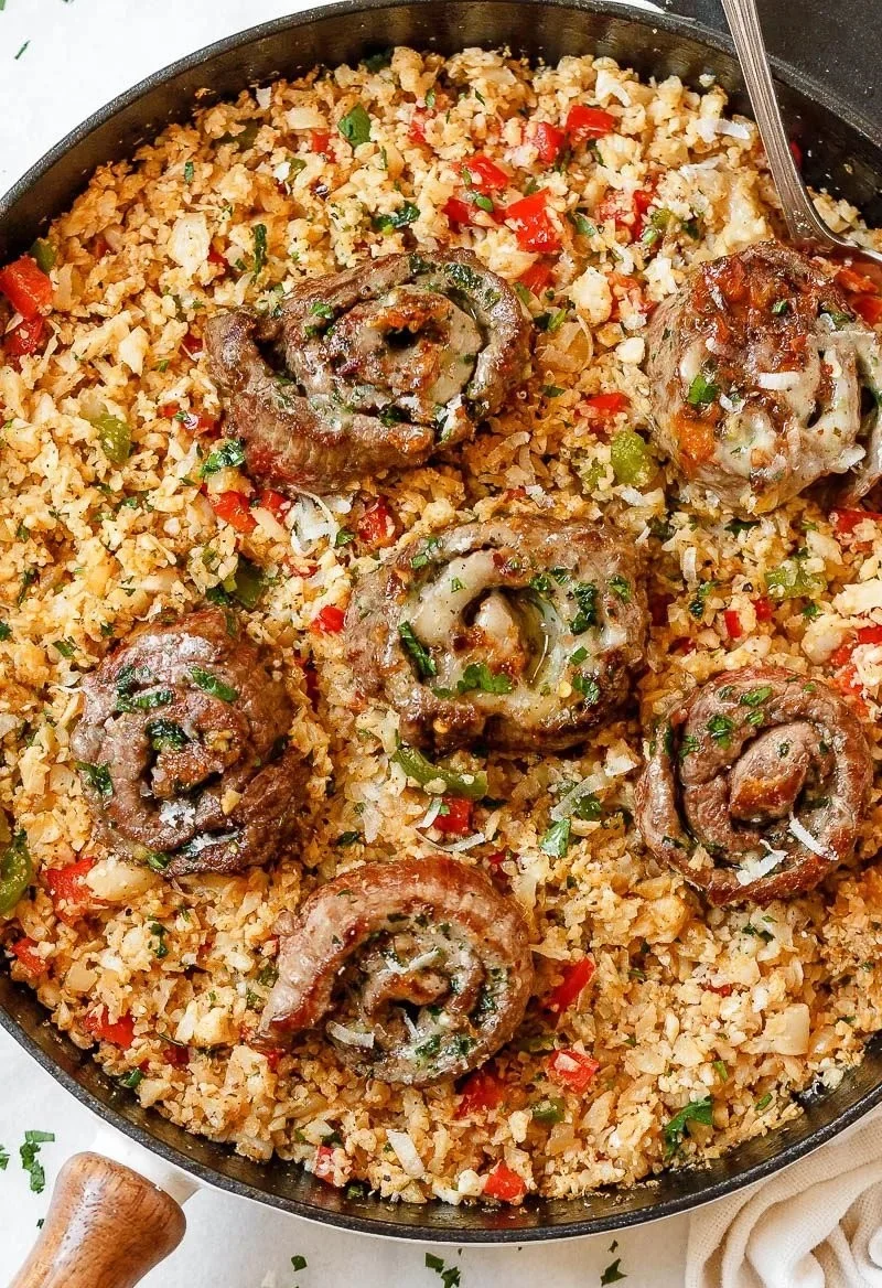 Mexican cauliflower rice served with cheesy steak roll ups on a plate