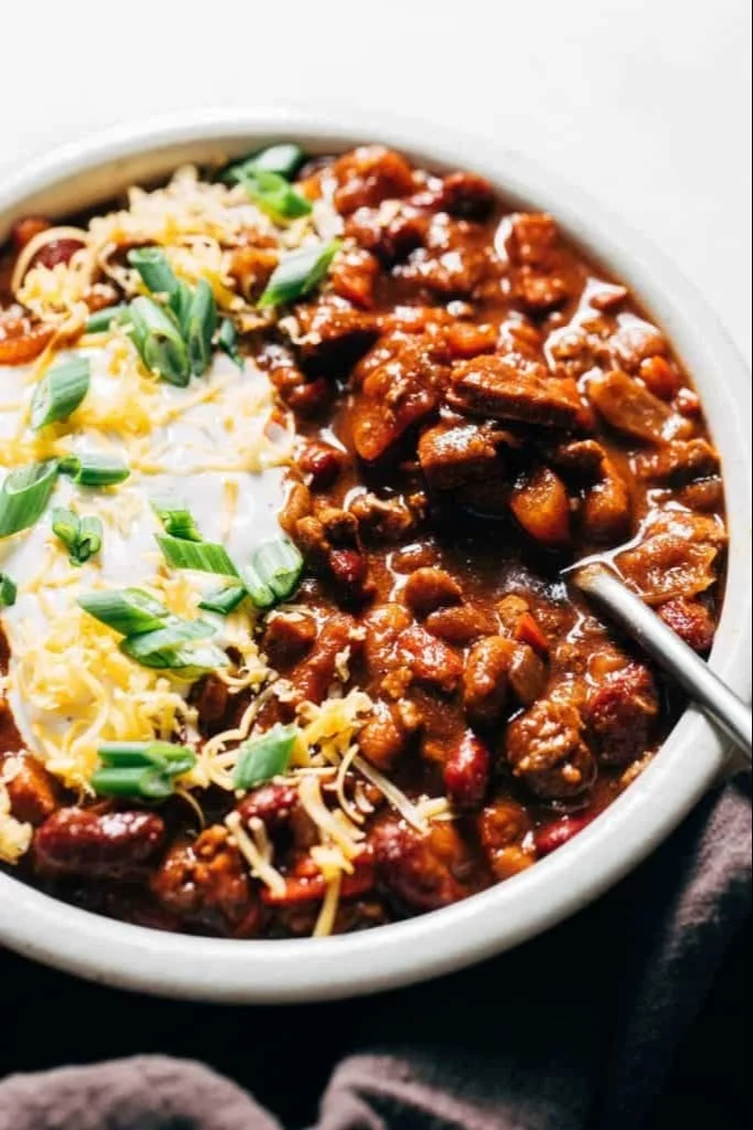 A bowl of Mom's Hearty Crockpot Chili garnished with cheese and herbs