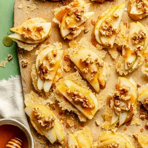 Parmesan Crusted Crostini topped with pear, walnuts, and hot honey served on a platter.