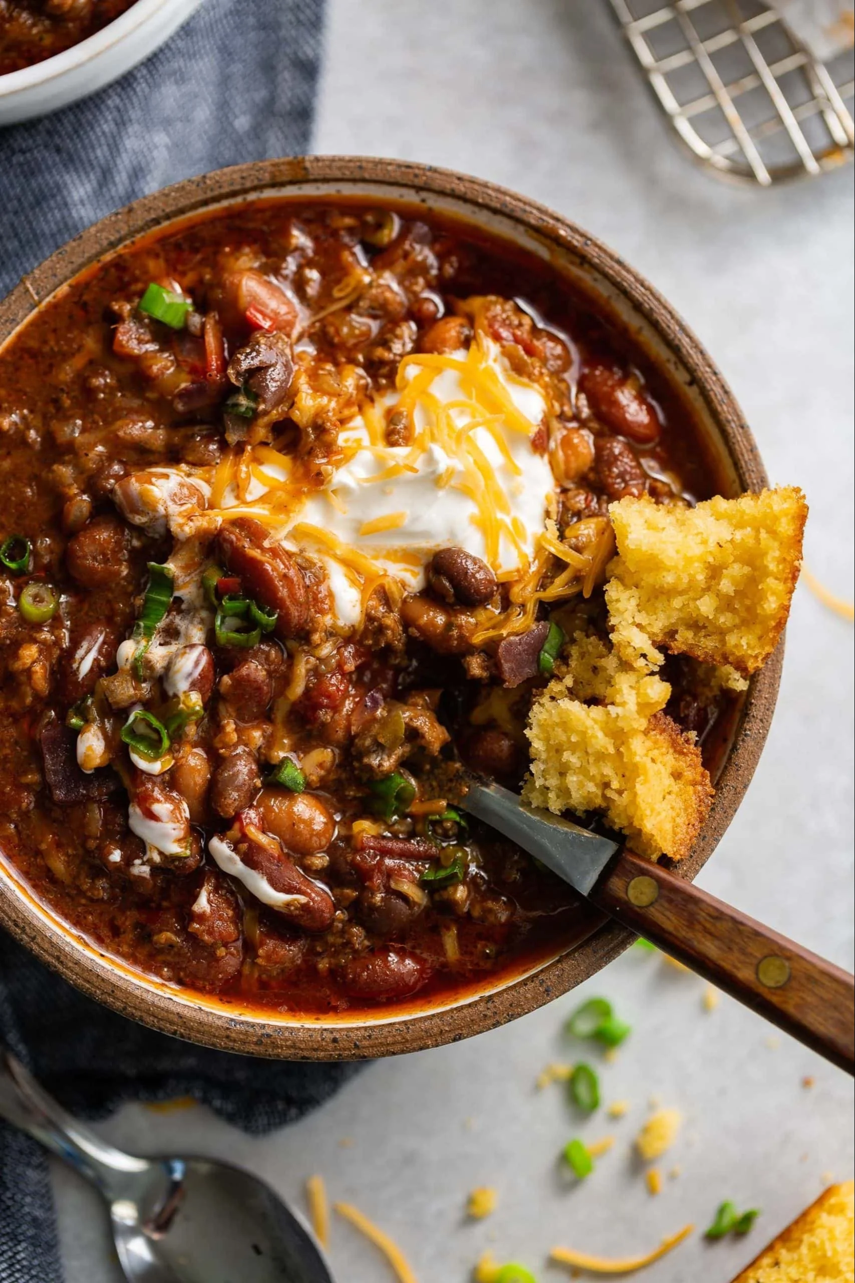 Bowl of rich and smoky chili topped with fresh herbs and served with cornbread.