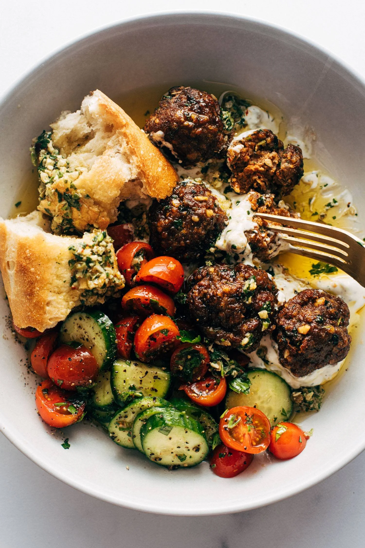 Sheet pan meatballs with tomato salad and zesty green sauce on a serving plate