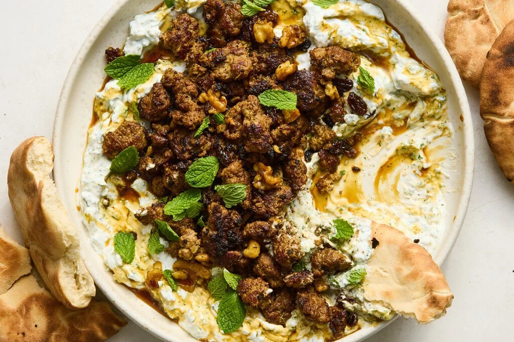 Smashed beef kebabs garnished with cucumber yogurt sauce on a platter.