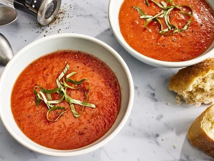 Bowl of homemade tomato soup garnished with fresh basil and served with bread.