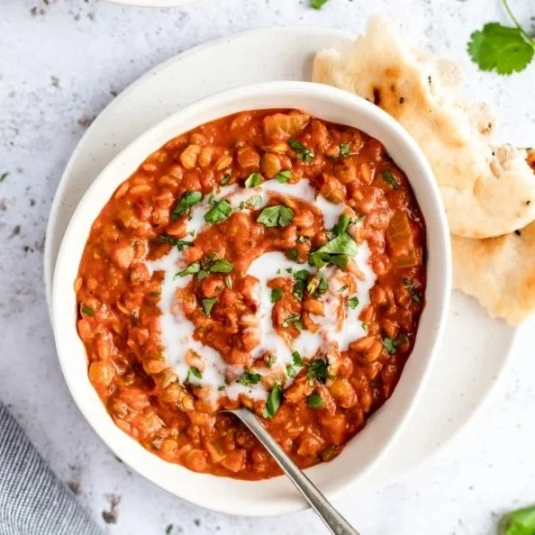 Bowl of Vegan Coconut Tomato Lentil Soup garnished with fresh herbs